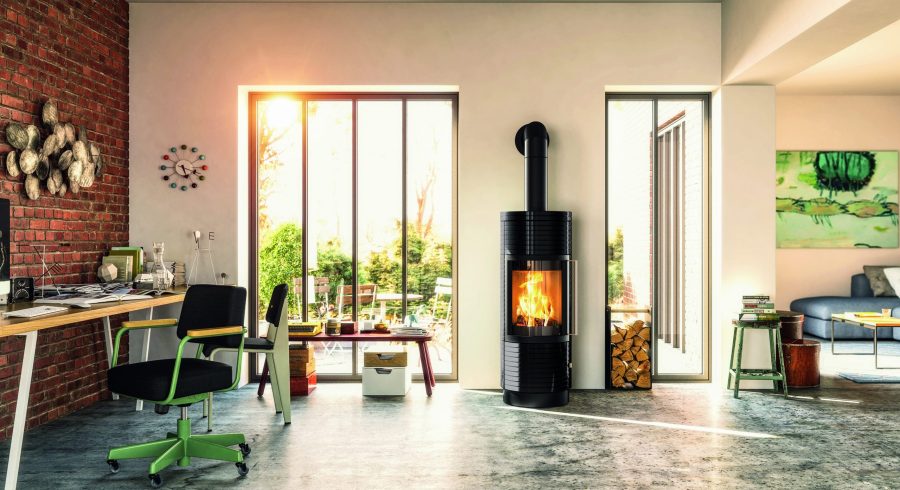 Wood stove in a living room with large windows and a small desk