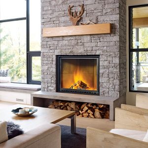 Wood fireplace in a large living room with large windows behind it and a comfortable seating area