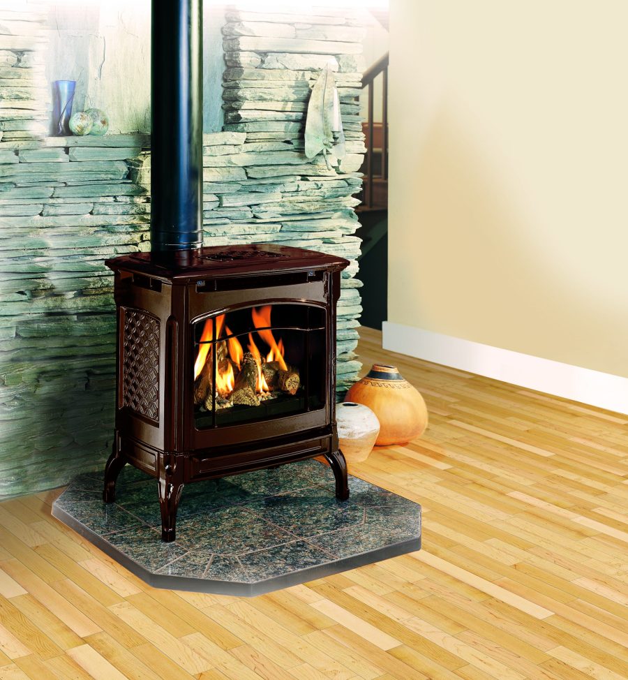 Black gas stove with stones behind it in a small room with wood floors