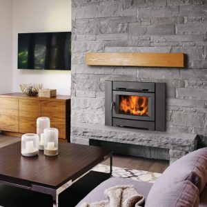 Wood fireplace insert in a stone chimney with comfortable furniture around it and a glass door