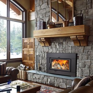 Large wood fireplace insert in a cabin with a stone surround and a large window in the background