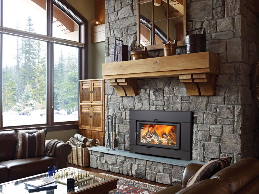 Large wood fireplace insert in a cabin with a stone surround and a large window in the background