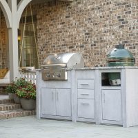 Outdoor kitchen built next to the entrance to a brick house with an arch support infront of the door