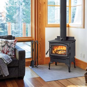 Wood stove in the corner of a living room with a large window and a comfortable looking couch