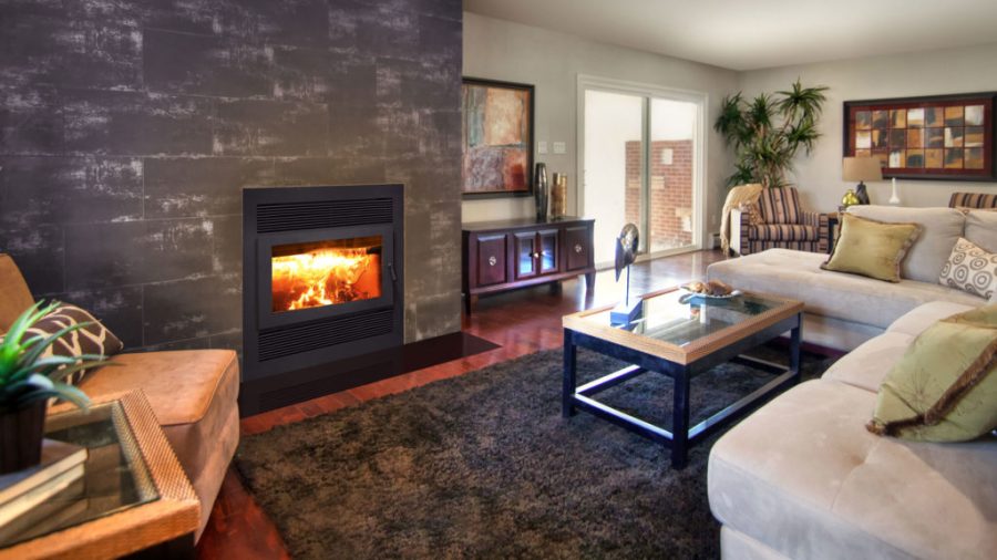 Wood fireplace insert in a home with a stone mantle and some seating with a glass door in the background