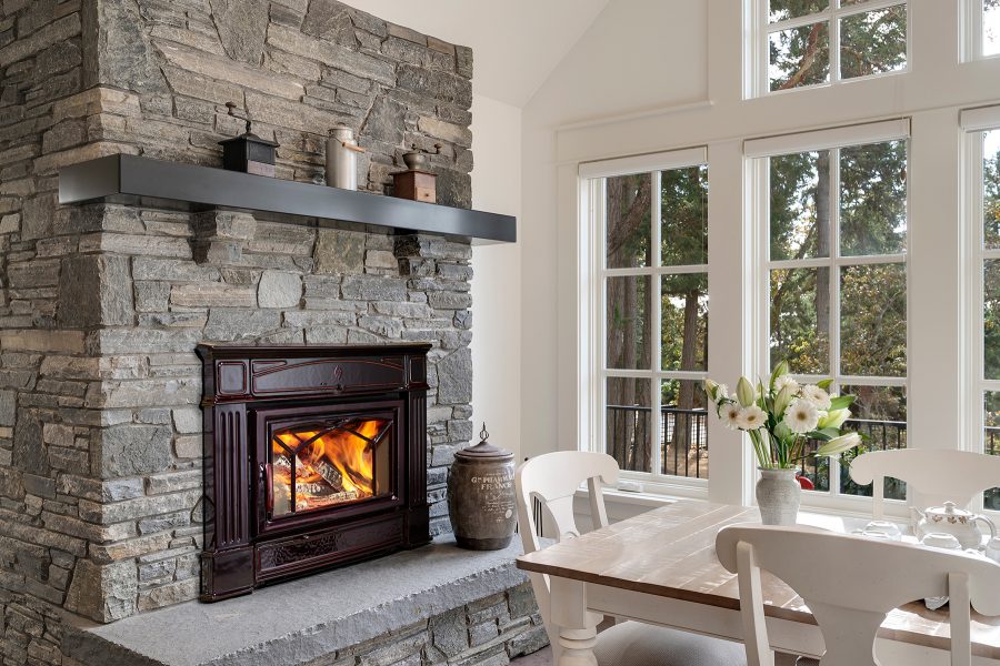 Black wood fireplace insert with a stone chimney, large windows in the background in a dining room