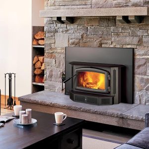 Wood fireplace insert in a stone wall in a small living room with logs next to it