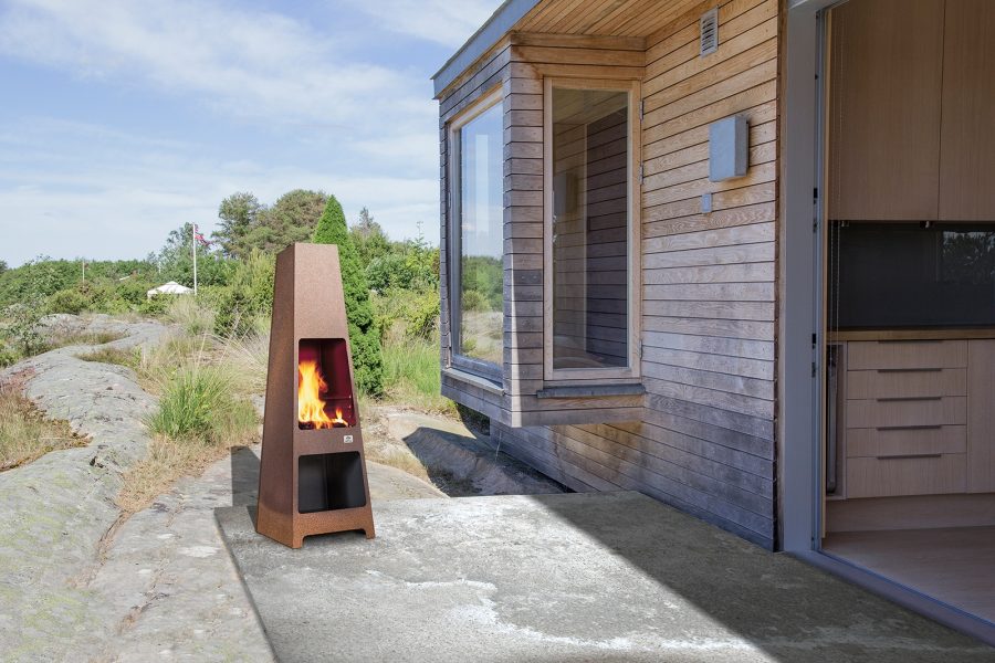 Outdoor wood fireplace next to a wood house with some grass in the background