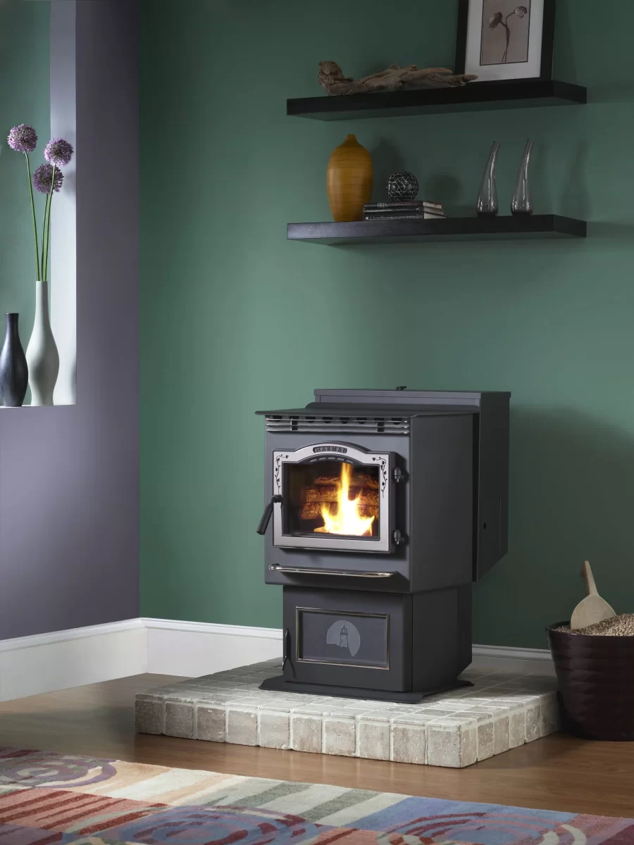 Black pellet stove in the corner of a room against a green wall with a large window next to it