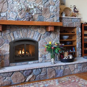 Fireplace insert surrounded by a large stone chimney in a living room with some shelves and a wood floor