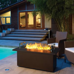 Outdoor gas fireplace table next to a pool with some seating and a set of stairs in the background