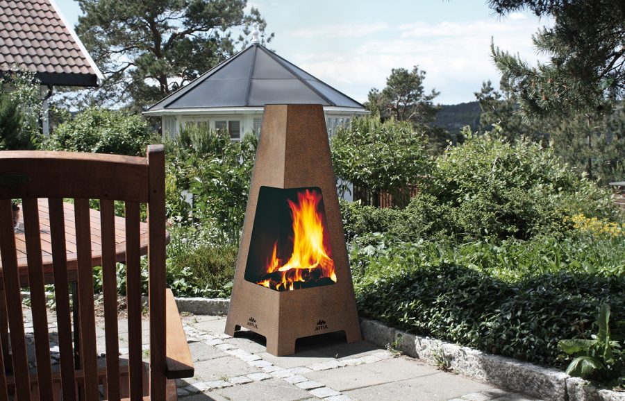 Picture of an outdoor wood fireplace with a green yard with trees behind it