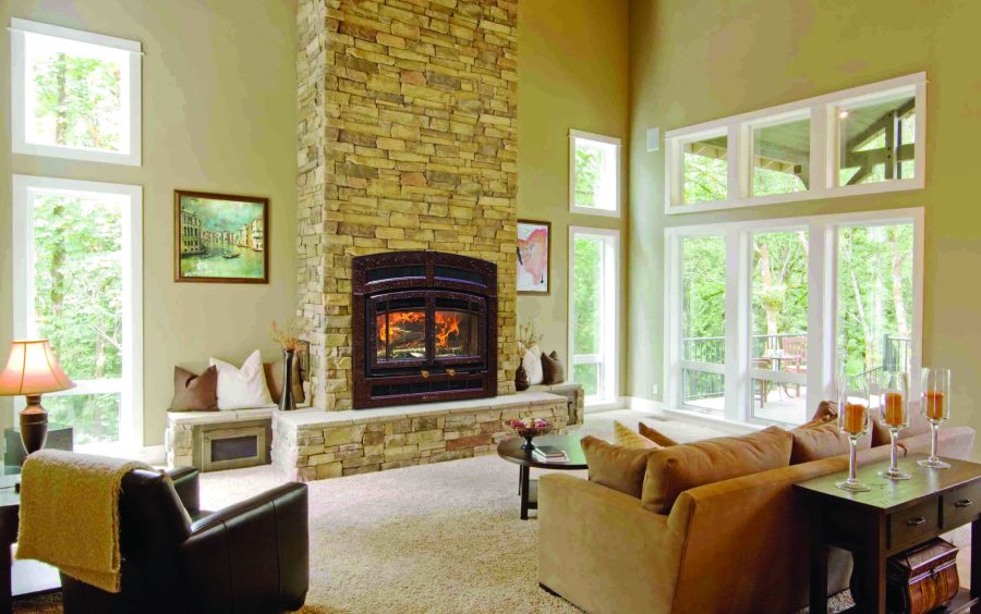 Wood fireplace insert in a living room with large windows showing a forest outside