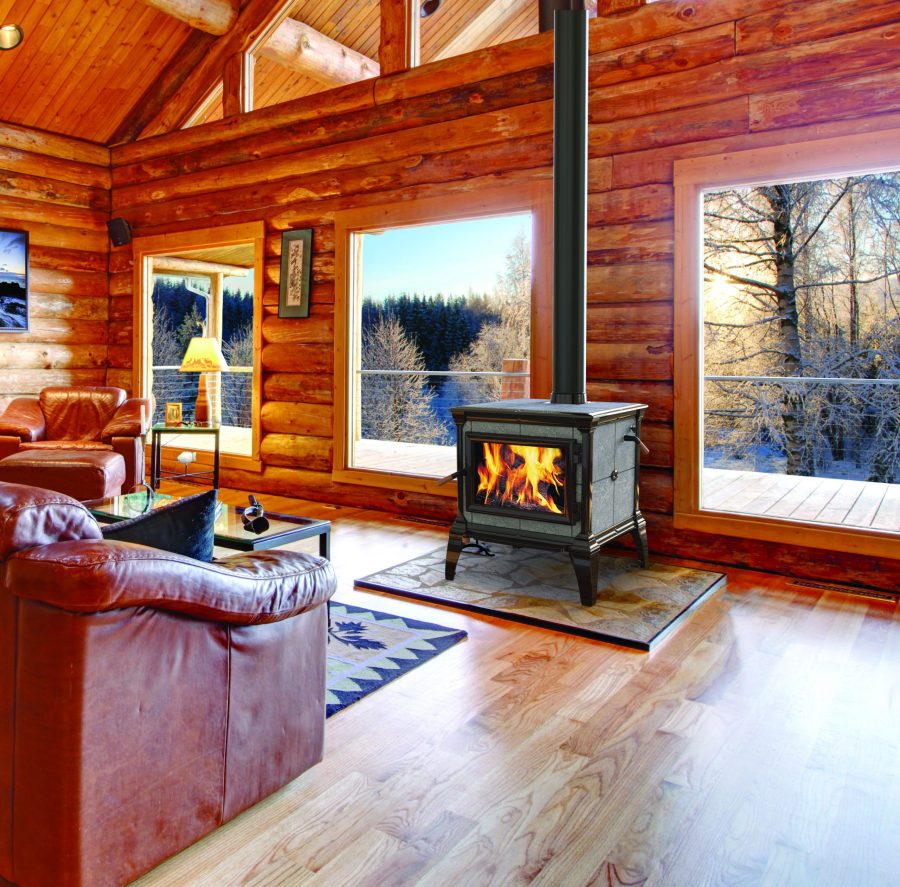 Small black wood fireplace in a log cabin with windows showing a snowy landscape with trees