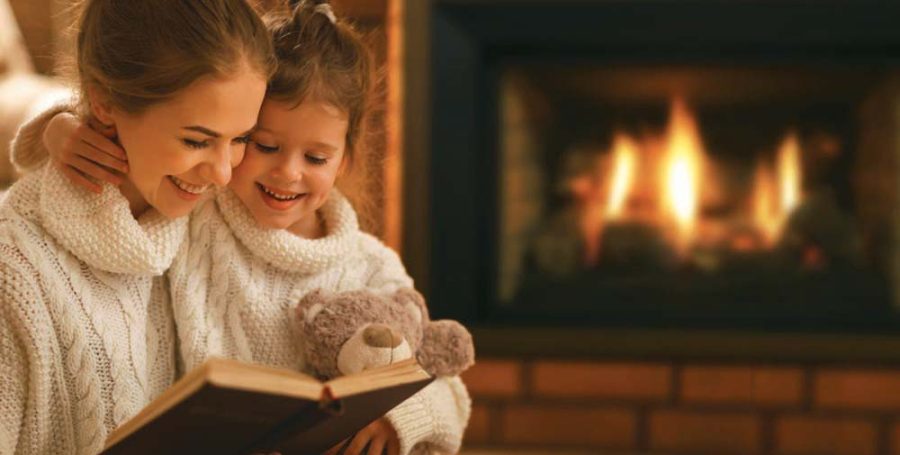 Two kids in warm sweater reading a book in front of a fire