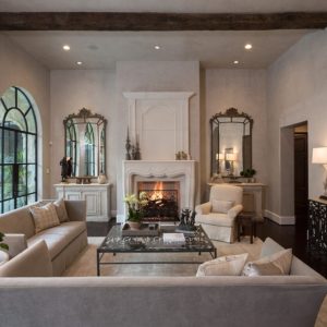 White living room with large windows and two mirrors on both sides of a fireplace with a fire going