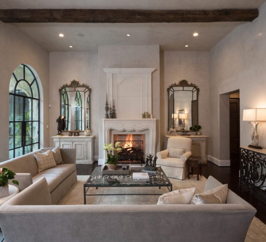 White living room with large windows and two mirrors on both sides of a fireplace with a fire going